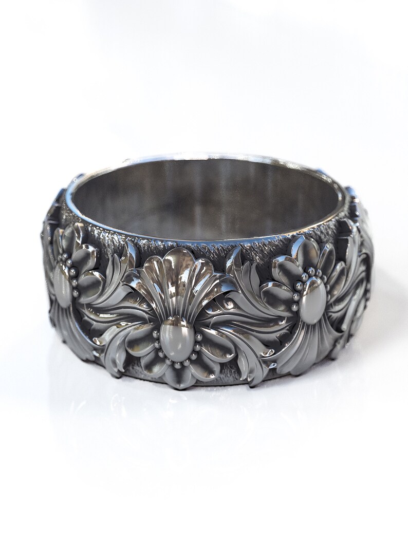 May include: A black metal ring with a floral design. The ring is wide and has a textured surface.
