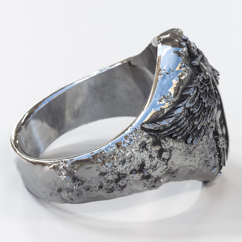 May include: A silver ring with a detailed design of a winged creature. The ring has a textured surface and a wide band.