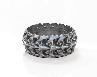 May include: A silver ring with a textured, geometric design. The ring is made of metal and has a shiny finish.
