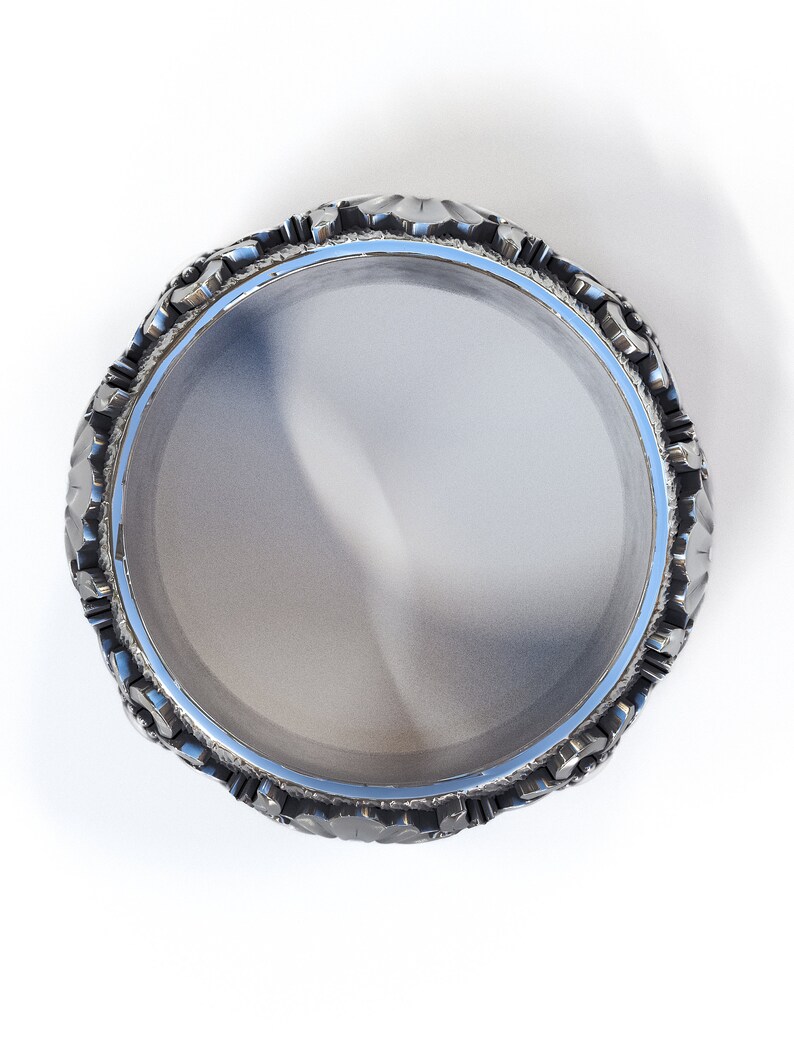 May include: A silver ring with a textured, ornate design around the band. The ring is circular and has a smooth, reflective surface.