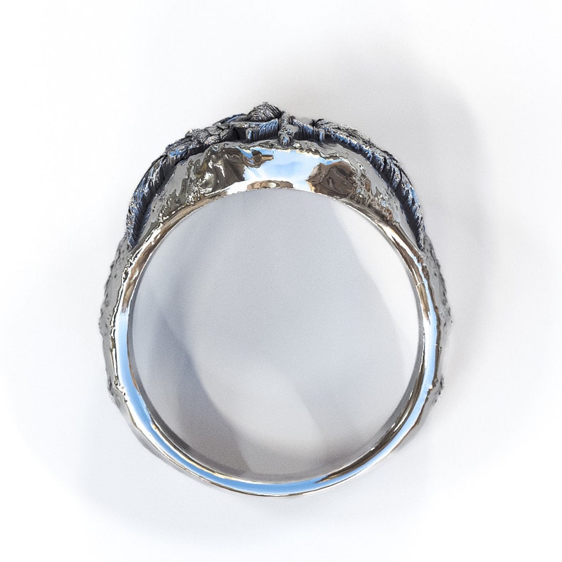 May include: A silver ring with a textured, organic design. The ring is wide and has a rounded band.