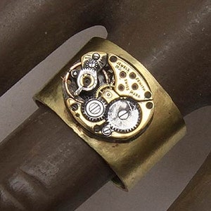 May include: A brass ring with a watch face embedded in the band. The watch face has silver gears and the text "Swiss Made" printed on it.