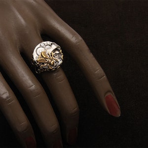Può includere: Un anello d'argento con un designo di insetto dorato. L'anello presenta un designo di orologeria dettagliato con ingranaggi e pignoni.