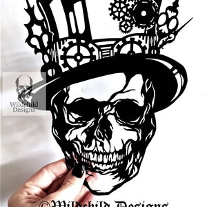 May include: Black and white silhouette of a skull wearing a top hat with gears and cogs. The skull is smiling and has a detailed design.