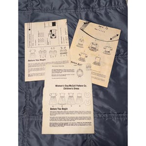 Puede incluir: Tres hojas de instrucciones de papel beige para un patrón de costura de vestido infantil de Woman's Day/McCall Pattern Co. Las hojas presentan texto impreso en negro, diagramas de estilos de vestidos, diseños de corte e instrucciones de montaje.