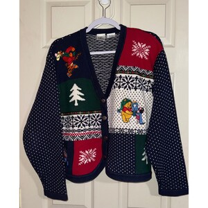 May include: A long-sleeve V-neck cardigan featuring a patchwork design with navy blue, red, white, and green sections. The knit garment displays embroidered Winnie the Pooh characters, white Christmas trees, and snowflake patterns with buttons.