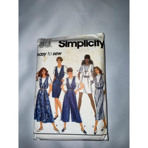 May include: A Simplicity sewing pattern envelope labeled 7877 and easy to sew. The front features illustrations of five different outfits including dresses, a jumpsuit, and a skirt set, all styled with white tops and blue or patterned bottoms.