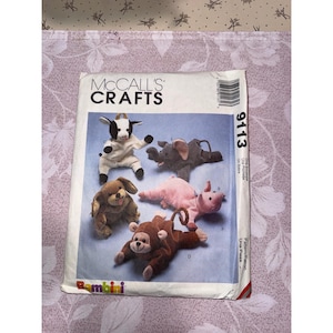 Può includere: Una busta di modelli McCall's Crafts con disegni di animali di peluche. Il modello include le istruzioni per creare una capra, un elefante, un cane, un maiale e una scimmia. La busta è etichettata "Bambini" e ha il numero di modello 9113.