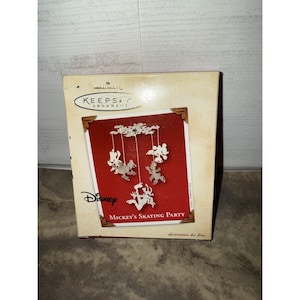 Peut inclure: Boîte d'ornement Hallmark Keepsake avec un fond rouge et un motif argenté de Mickey Mouse patinant. La boîte porte le logo Disney et le texte "Mickey's Skating Party". La boîte est beige avec des coins bruns.