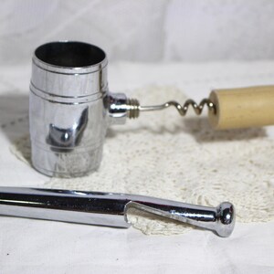 May include: A chrome-plated wine bottle opener set. The set includes a barrel-shaped corkscrew with a wooden handle, and a bottle opener. The items are displayed on a white lace doily.