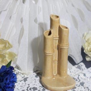 May include: A beige ceramic vase with a bamboo design. The vase has three openings and a rounded base. The vase is approximately 6 inches tall.