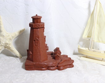May include: A brown decorative lighthouse figurine with a small house attached, set on a rocky base. A white starfish and a small yellow sailboat are also present, suggesting a nautical theme.