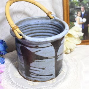 May include: A blue and black ceramic vase with a bamboo handle. The vase has a textured surface and a unique design.