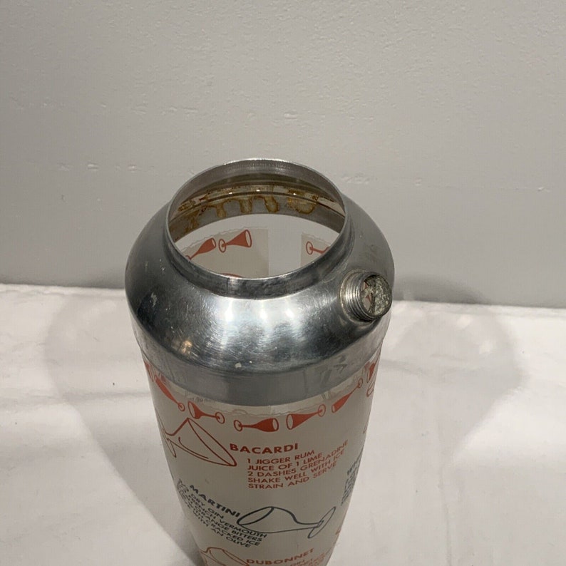 May include: A silver cocktail shaker with a glass interior and a printed recipe for a Bacardi cocktail. The recipe includes 1 jigger rum, juice of 1 lime, 2 dashes grenadine, shake well with ice, strain and serve.