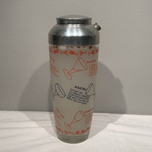 May include: A vintage silver cocktail shaker with a glass body and a printed recipe for a Martini, Bacardi, Side Car, and Dubonnet. The recipes are printed in orange and black text on a white background.