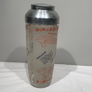 May include: A silver cocktail shaker with a glass body featuring instructions for making the Manhattan and Alexander cocktails. The instructions are printed in orange and blue on a cream background.