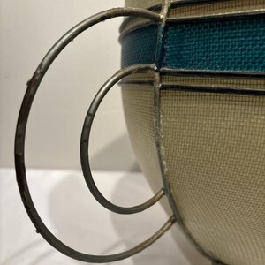 May include: A vintage-style decorative bowl with a woven beige exterior and a teal band. The bowl features a metal frame and handle, adding a touch of retro charm. The design is reminiscent of mid-century modern decor.