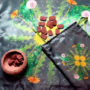 May include: A green cloth with a dandelion pattern and a set of runes in a small brown bowl and a pouch.
