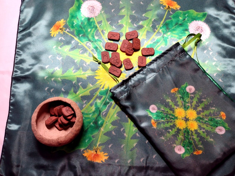 May include: A green cloth with a dandelion pattern and a set of runes in a small brown bowl and a pouch.