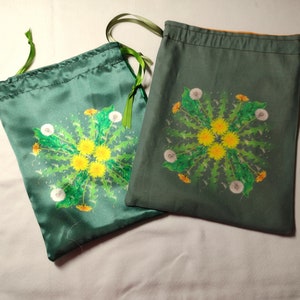 May include: Two green drawstring bags with a dandelion design. The bags are made of a soft, silky fabric and have a green drawstring.