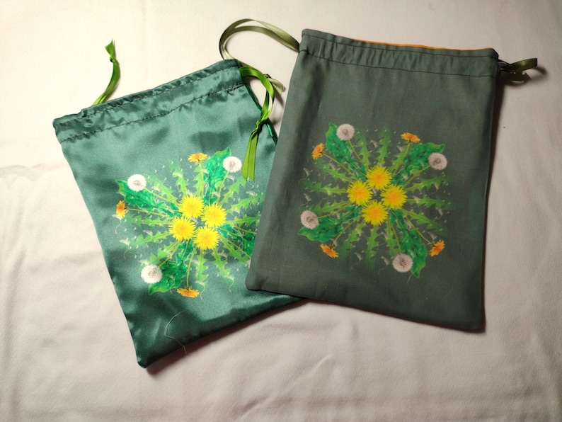 May include: Two green drawstring bags with a dandelion design. The bags are made of a soft, silky fabric and have a green drawstring.