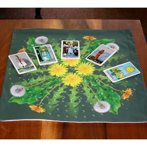 May include: A green tarot cloth with a dandelion design. Five tarot cards are laid out on the cloth. The cards are: The Chariot, The Tower, The Sun, The Magician, and Six of Swords.