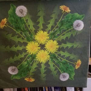 May include: A green canvas print with a symmetrical design of dandelion flowers and seed heads. The flowers are yellow and white, and the seed heads are white and fluffy. The background is a dark green.