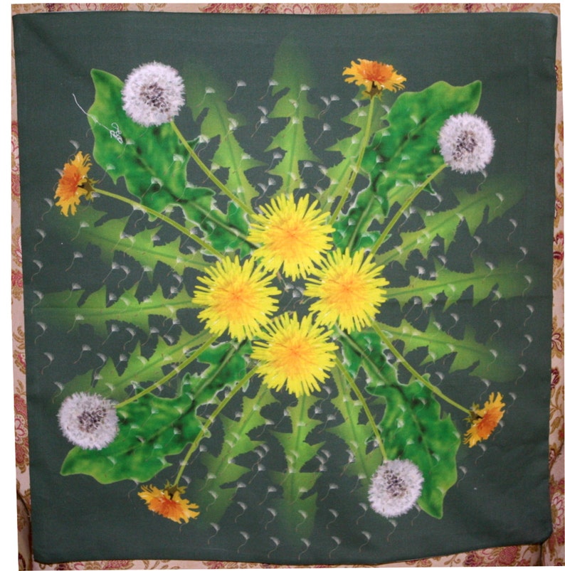 May include: A green fabric square with a symmetrical design of yellow dandelions and white dandelion seeds. The design is surrounded by green leaves.