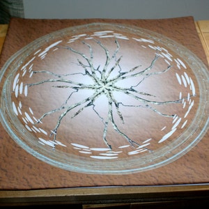 May include: A brown fabric coaster with a circular design featuring a white crackled pattern and a light blue border.
