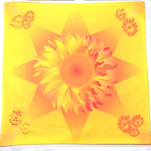 May include: A yellow square fabric with a large orange and red sunflower in the center. The sunflower has a yellow center and is surrounded by a six-pointed star. There are four smaller yellow flowers in the corners of the square.
