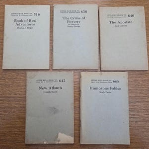 May include: Five vintage Little Blue Books are displayed, each with a unique title and author. The titles include "Book of Real Adventures," "The Crime of Poverty," "The Apostate," "New Atlantis," and "Humorous Fables."