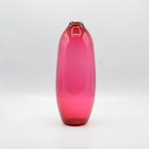 May include: A tall, oval-shaped vase in a vibrant shade of pink. The glass vase has a smooth, glossy finish and a slightly flared opening. The color is consistent throughout, with a deeper hue at the base.