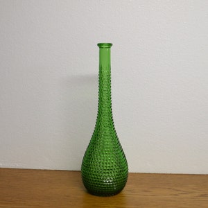 May include: A tall, green glass vase with a textured, diamond-patterned surface. The vase has a long, slender neck and a rounded base. The vase is approximately 12 inches tall.