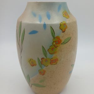 May include: A beige ceramic vase with a floral design. The vase features yellow and orange flowers with green leaves, blue accents, and a speckled texture. The vase has a rounded shape.