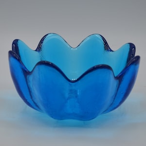 May include: A vibrant blue glass bowl with a unique, scalloped edge design. The bowl's interior is a lighter shade of blue, creating a striking contrast. This decorative piece is ideal for serving or display.