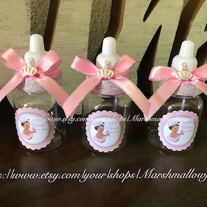 May include: Three clear baby bottle-shaped containers with white nipples, adorned with pink ribbons, silver trim, and gold crowns. Each bottle has a pink label with a baby graphic and the text "A little Princess is on her way."
