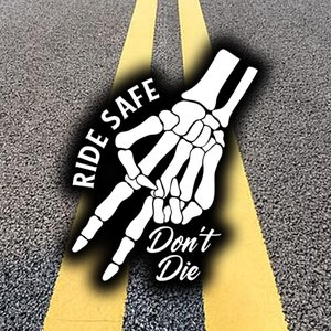 May include: A white skeleton hand with the words "Ride Safe" and "Don't Die" on a black background. The image is on a gray asphalt surface with yellow lines.