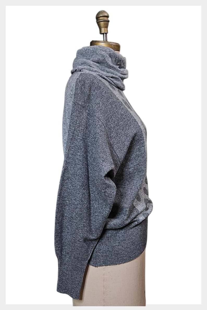 May include: A grey turtleneck jumper with long sleeves. The jumper has a textured knit and a high, folded collar. The sleeves are long and the overall style is casual. The jumper is displayed on a mannequin.