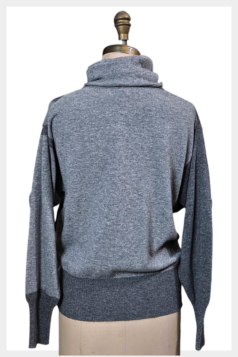 May include: A grey turtleneck jumper with long sleeves. The jumper has a ribbed hem and cuffs, and the sleeves are a darker shade of grey. The jumper is displayed on a mannequin.