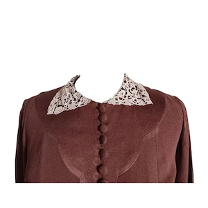 Op de afbeelding: Een effen bruine blouse met lange mouwen en een puntige kraag met gedetailleerd cr&egrave;mekleurig kant. Het kledingstuk is voorzien van een verticale rij bijpassende met stof beklede knopen aan de voorzijde en een gebogen pasnaad op de borst.