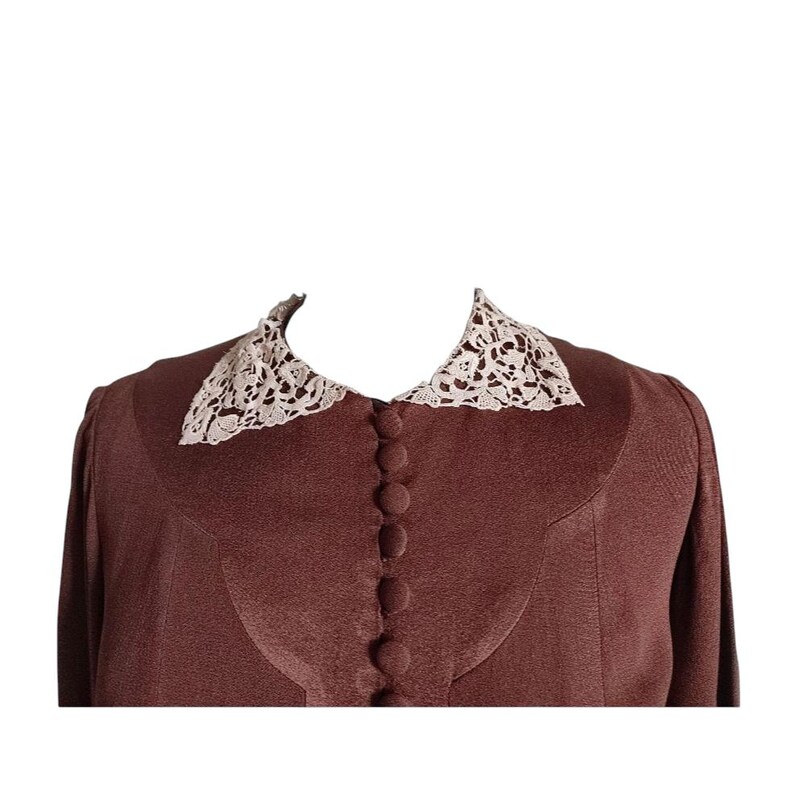 Op de afbeelding: Een effen bruine blouse met lange mouwen en een puntige kraag met gedetailleerd cr&egrave;mekleurig kant. Het kledingstuk is voorzien van een verticale rij bijpassende met stof beklede knopen aan de voorzijde en een gebogen pasnaad op de borst.