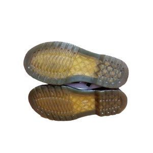 May include: Close-up of the bottom of a pair of black leather boots with yellow rubber soles.