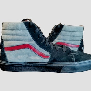 May include: High-top sneakers in black and gray with a red side stripe. The shoes have a black sole and laces. The upper part of the shoe is gray with a textured design.