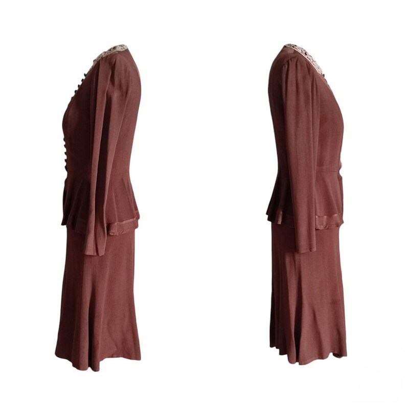 Op de afbeelding: Een tweedelig bruin rokpak bestaande uit een jasje met lange mouwen en een peplum-taille, een rij kleine knoopjes aan de voorzijde en een decoratieve kanten kraag. De bijpassende rok is knielang met een uitlopende zoom en een gladde textuur.