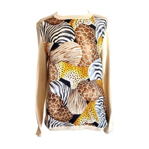 May include: Beige long-sleeved sweater with a vibrant animal print design on the front. The print features a collage of zebra stripes, giraffe spots, and leopard patterns. The sweater has a round neckline.