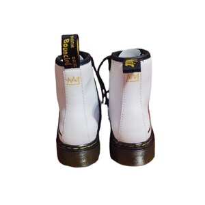 May include: White leather ankle boots with black laces and a black and yellow sole. The boots have a gold crown logo on the side and the text "SOLES WITH BOUNCING" on the back.