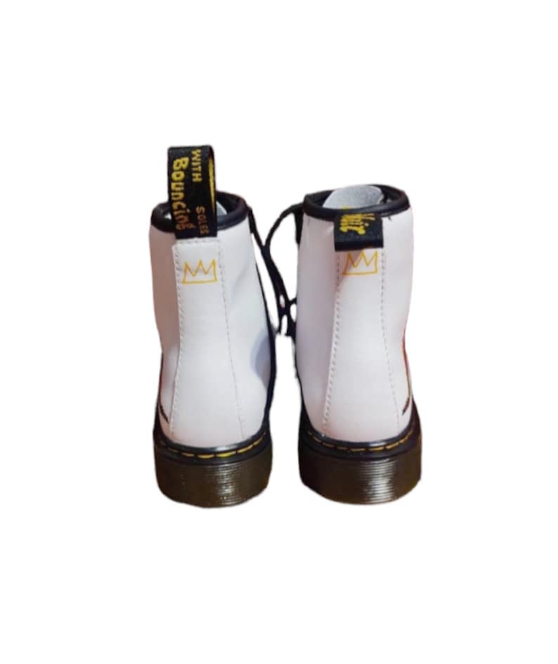 May include: White leather ankle boots with black laces and a black and yellow sole. The boots have a gold crown logo on the side and the text "SOLES WITH BOUNCING" on the back.