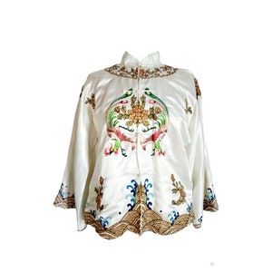 May include: A white silk jacket with a mandarin collar and intricate embroidery of peacocks and flowers. The jacket has a gold and blue trim around the bottom.