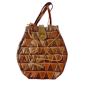 Könnte beinhalten: Eine braune Lederhandtasche mit geometrischem Design. Die Tasche hat eine Reihe von dreieckigen Patches in verschiedenen Brauntönen. Sie hat einen oberen Griff, einen Kordelzugverschluss und eine dekorative Quaste.