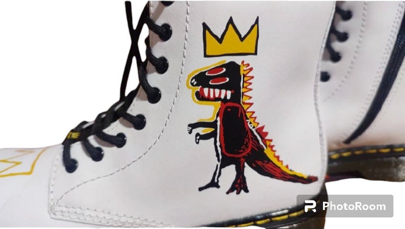 May include: White leather boots with black laces and a yellow crown and red, black, and yellow dinosaur graphic.